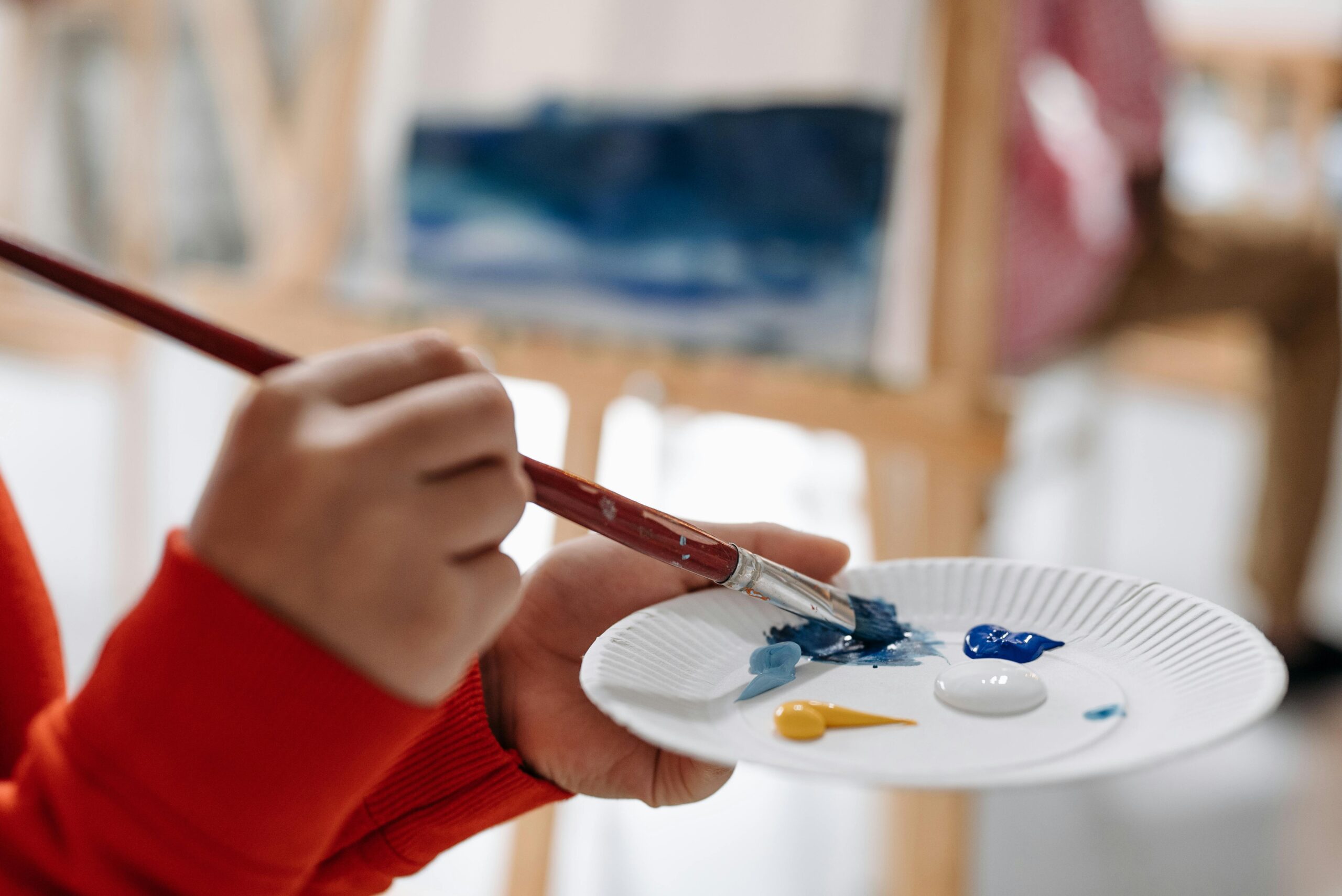 Close-up of a person mixing paints on a paper plate with a brush during a painting session.